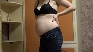 Milf grávida tira a calça jeans justa, veste uma roupa sexy e masturba a boceta peluda com um vibrador. fetiche caseiro e espólio suculento com um cu cabeludo.